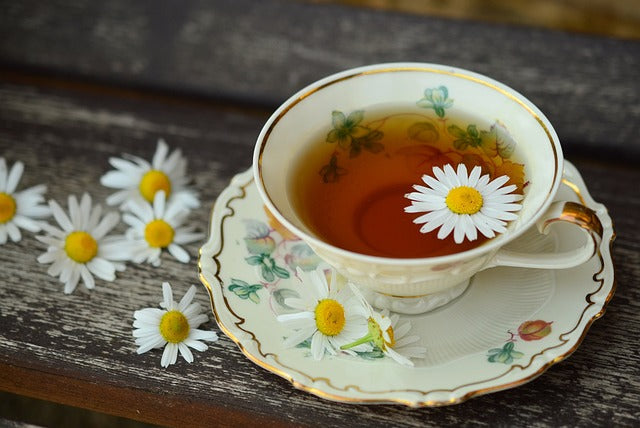 Loose leaf herbal tea in a floral cup with chamomile blossoms