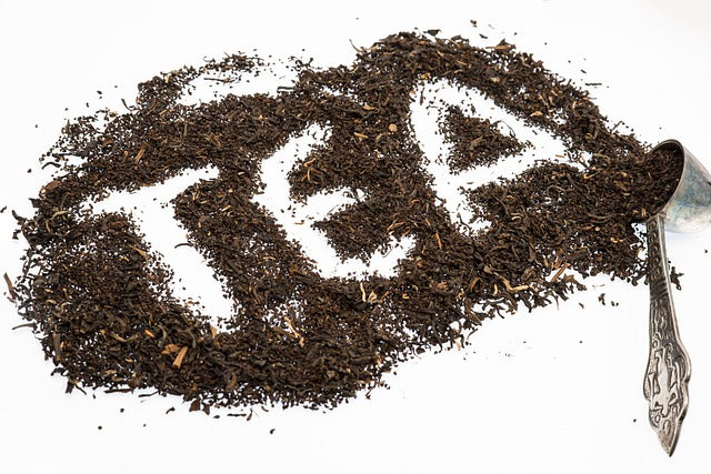 Loose-leaf black tea leaves arranged to spell the word TEA on a white surface, with a vintage silver spoon