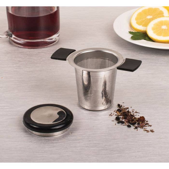 Stainless steel tea infuser with loose tea leaves on a table.