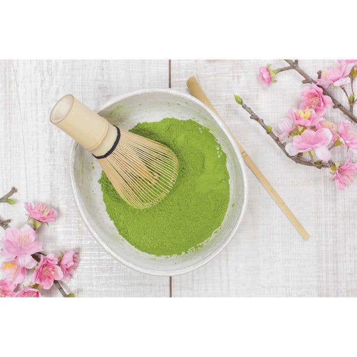 Matcha green tea powder in a bowl with a whisk, cherry blossoms on a white background