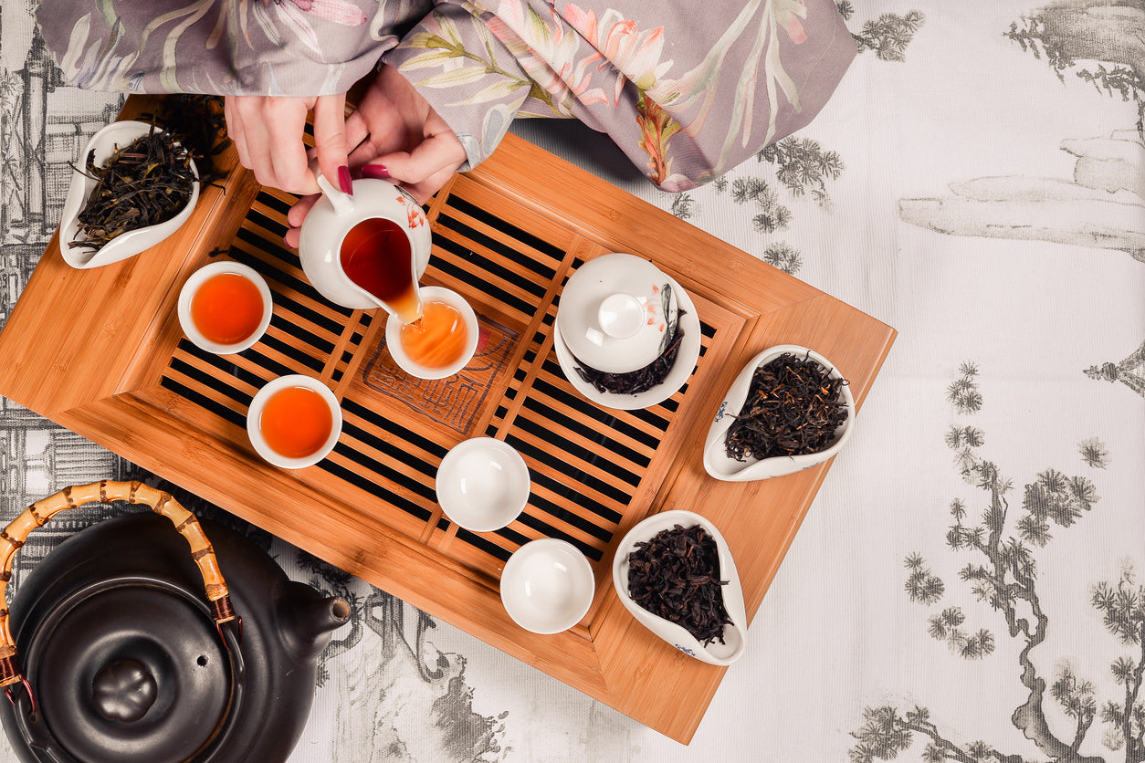 Gong Fu tea-making setup with a wooden tray, teapot, and tea leaves on a decorative tablecloth.