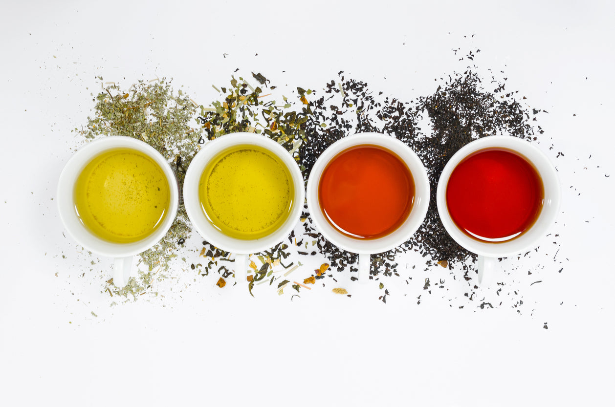Four white bowls with different colored tea and corresponding dry tea leaves on a white background